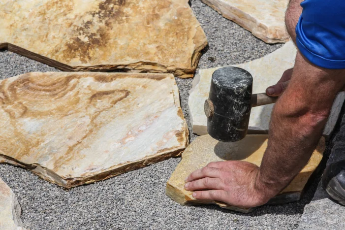 Person verlegt Steinplatte mit Gummihammer